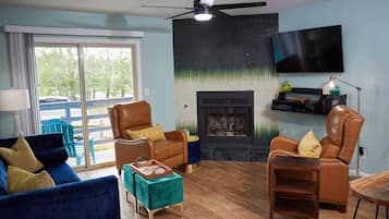 A living room with a fireplace, leather armchairs, a blue sofa, and a television mounted on the wall.