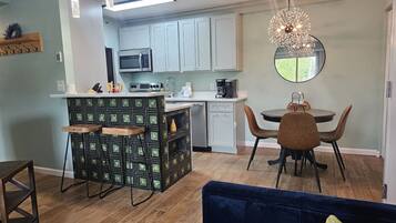 A modern kitchen with light blue cabinets, a central island with stools, a dining area with a round table and chairs, and a large mirror above the dining table.