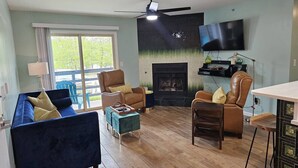 Ein Wohnzimmer mit blauem Sofa, braunem Ledersessel, Couchtisch aus Holz und Kamin.