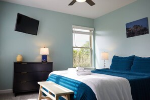 A bedroom with a bed, bedside tables, a desk, a window, and a wall-mounted TV.
