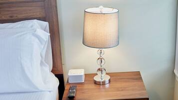 A neatly made bed with white linens, a bedside table with a lamp, a remote control, and a small white device.