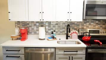 A kitchen with white cabinets, a stainless steel dishwasher, a microwave, and a red kettle.