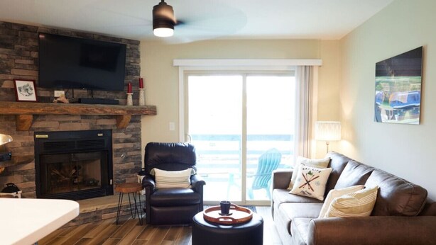 Una sala de estar con chimenea de piedra, sillón de cuero y sofá con vistas al exterior.
