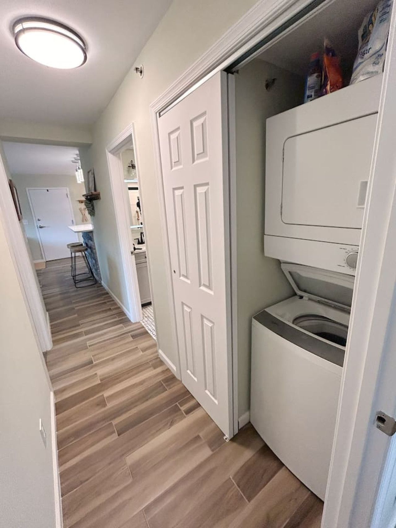 A laundry room with a washing machine and dryer, a wooden floor, and a white door.