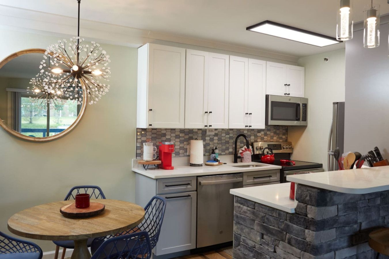 A modern kitchen with white cabinets, a microwave, a dishwasher, and a stone accent wall.