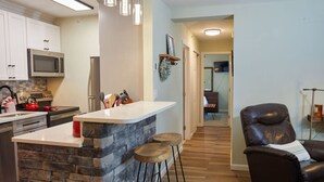 Una cocina moderna con una isla de piedra, taburetes de bar y una butaca de cuero negro.