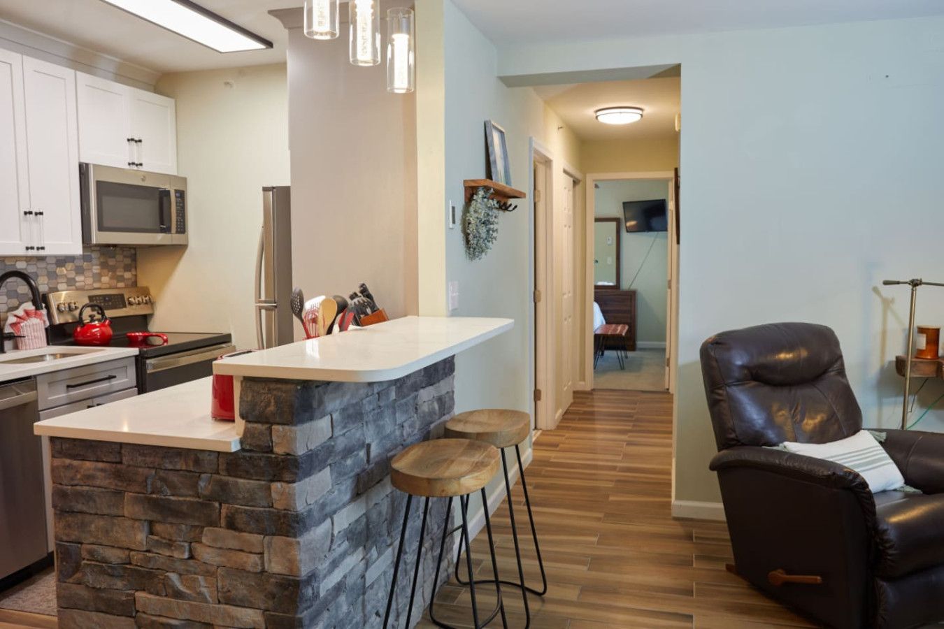 Een moderne keuken met een stenen kookeiland, barkrukken en een zwarte leren fauteuil.