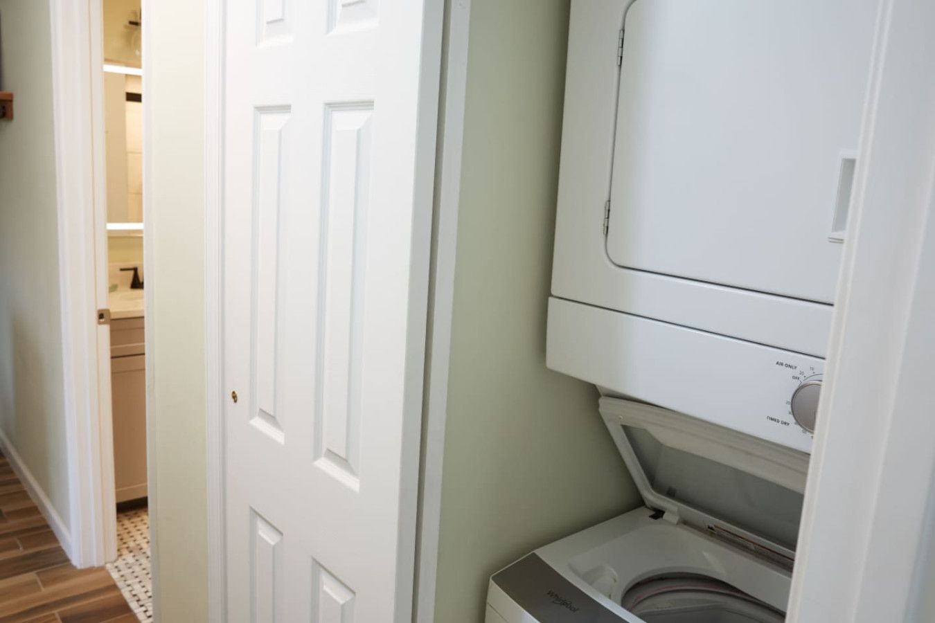 Een wasserette met een gestapelde wasmachine en droger, een witte deur en een zichtbaar aanrecht met een kraan.