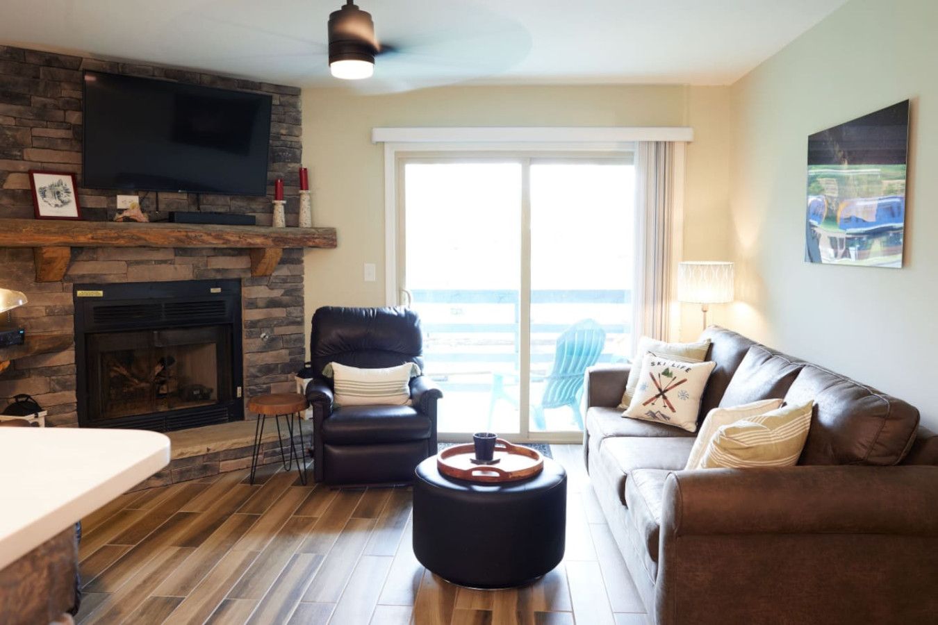 A living room with a stone fireplace, leather armchair, and a sofa with a view to the outside.