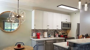Una cocina moderna con armarios blancos, microondas, lavavajillas y una pared decorativa de piedra.