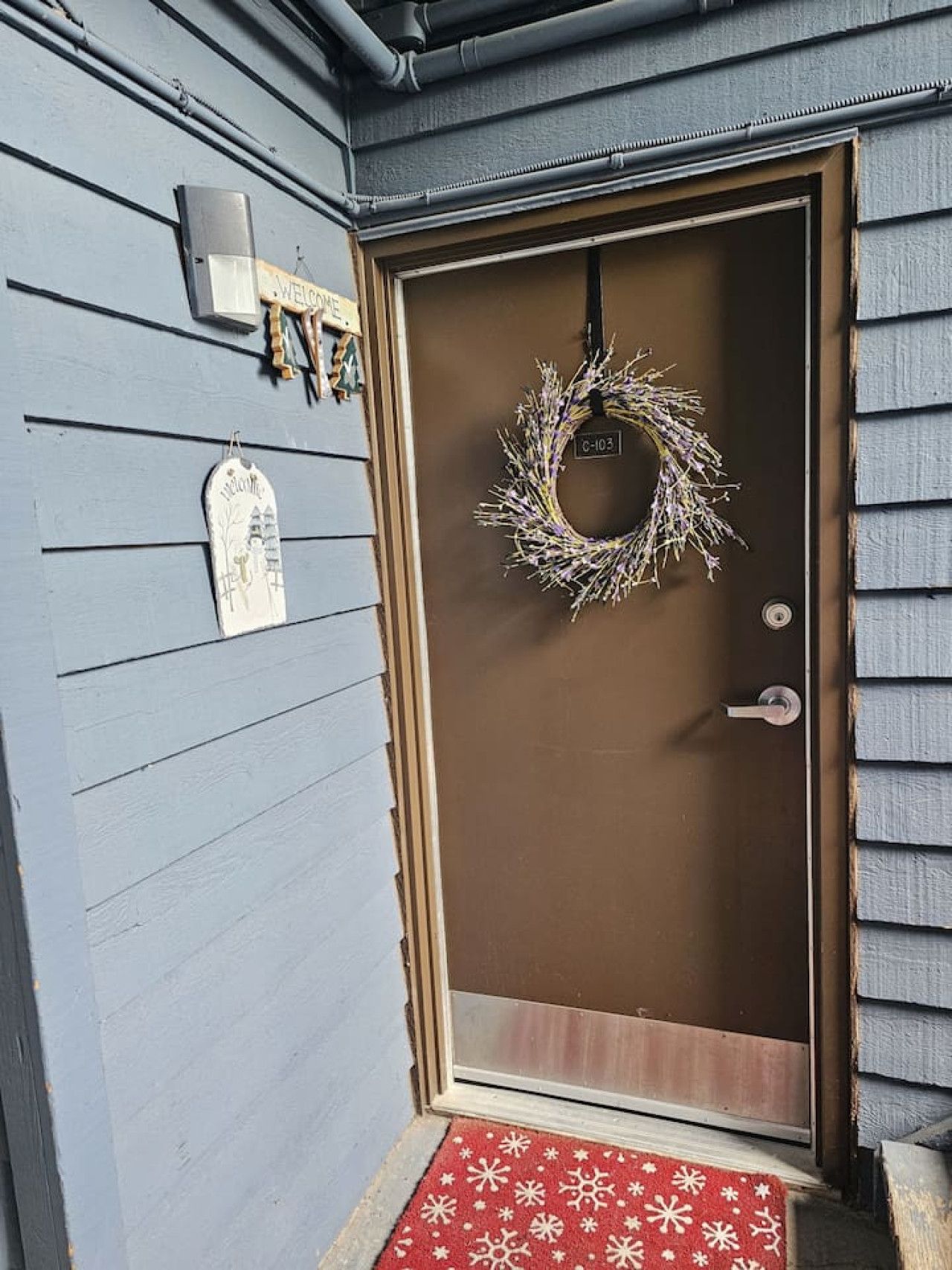 A front door with a wreath, a welcome sign, and a doormat.