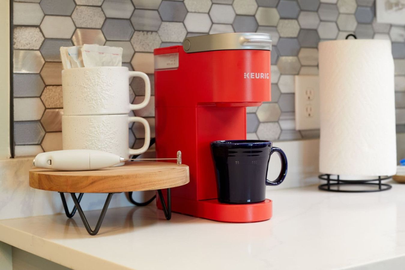 A red Keurig coffee maker on a kitchen counter with a white mug and a white coffee pod.