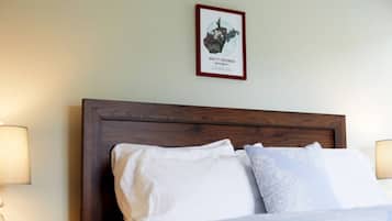 A neatly made bed with white linens and a wooden headboard. A framed map of West Virginia hangs on the wall above the bed.