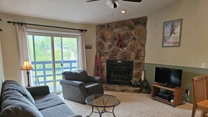 A living room with a stone fireplace, a television on a wooden stand, and a sofa set.