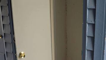 A closed door with a brass doorknob, a small step leading up to it, and a grey exterior wall with siding.