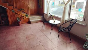 Una habitación con una escalera de madera, una pequeña mesa con sillas y un ventanal con cortinas.