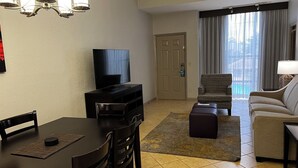 A hotel room with a dining area, a TV, a sofa, and a view of a pool. - Family Vacation Getaway (Kissimmee)