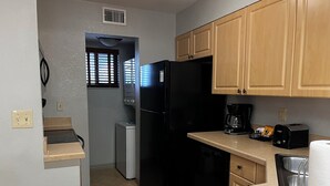 A compact kitchen with wooden cabinets, a black refrigerator, a coffee maker, and a dishwasher. - Family Vacation Getaway (Kissimmee)