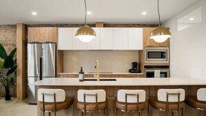 Una cocina moderna con una isla central, taburetes de bar, electrodomésticos de acero inoxidable e iluminación colgante.
