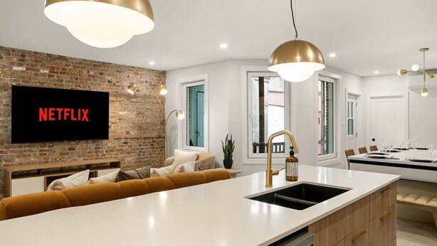 Cocina moderna con una isla central, horno empotrado y un televisor grande montado en una pared de ladrillo.