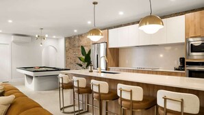 Una cocina moderna con una isla central, taburetes de bar, iluminación colgante y una pared de ladrillo decorativa.