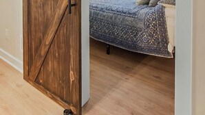 Una habitación con una puerta de madera estilo granero, una cama con ropa de cama estampada, un ventilador de techo y un cuadro en la pared.