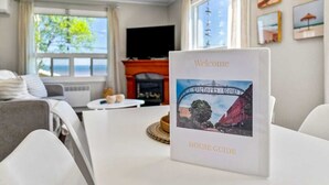 Moderni olohuone, jossa on valkoinen sohva, sohvapöytä ja takka. Pöydällä on tervetulotoivotuskyltti, jossa on kaupunkikuva.