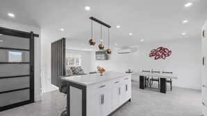 A modern kitchen with a central island, pendant lights, and a dining area with a table and chairs. - Family Retreat  – King Bed, Jacuzzi & Big Backyard (Charlottetown)