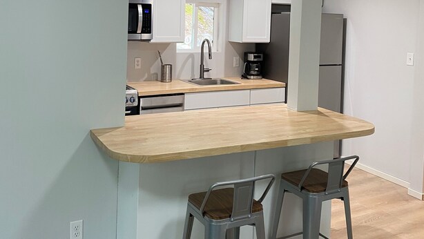 A modern kitchen with a wooden ceiling, white cabinets, a central island with bar stools, and a visible window. - Cozy cabin with WiFi in charming Au Train, Completely remodeled as of June 2025 (Au Train)