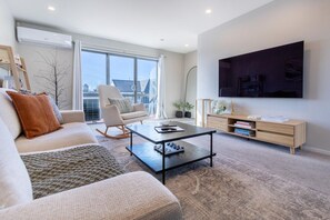 A modern living room with a sofa, a rocking chair, a coffee table, and a TV mounted on the wall.