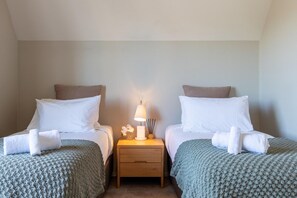 A hotel room with two beds, a nightstand with a lamp, and a small table with a vase of flowers.