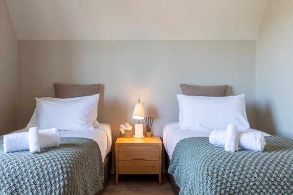 A hotel room with two beds, a nightstand with a lamp, and a small table with a vase of flowers.