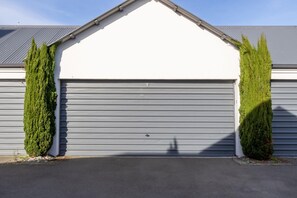 A garage with a white door and grey shutters, flanked by two tall, green, coniferous trees.
