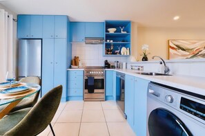 A modern kitchen with blue cabinets, a stainless steel refrigerator, and a built-in dishwasher.