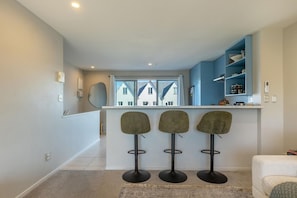Una cocina moderna con barra, tres taburetes y vista a edificios.