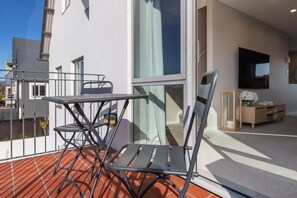 Ein moderner Balkon mit Glastür, einem Metalltisch und zwei Stühlen.