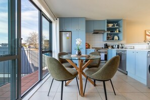Une cuisine moderne avec des meubles bleus, un coin repas avec une table en verre et quatre chaises, et un balcon avec vue.