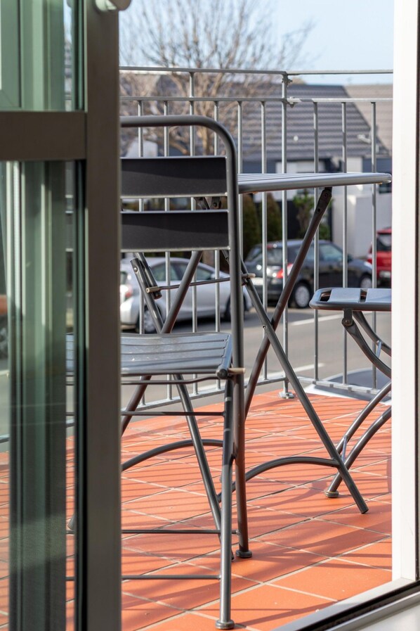 A metal chair and table outside a building with a tiled floor and a metal railing in the background.