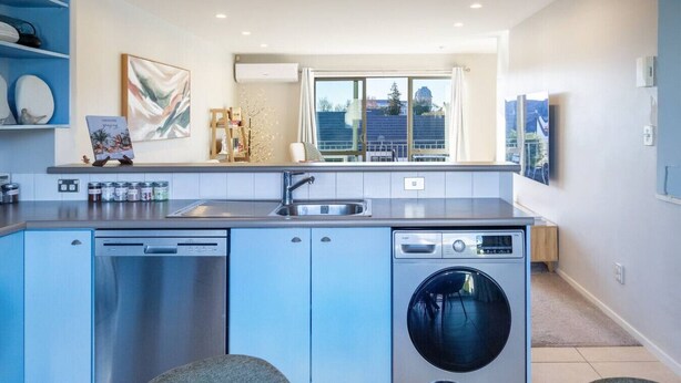 A modern kitchen with a dishwasher, washing machine, and a large window providing natural light. - Casino Margaret Mahy  2bd garage (Christchurch)