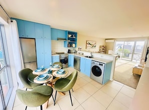 A modern kitchen with blue cabinets, a dining area with green chairs, and a view of the outside.