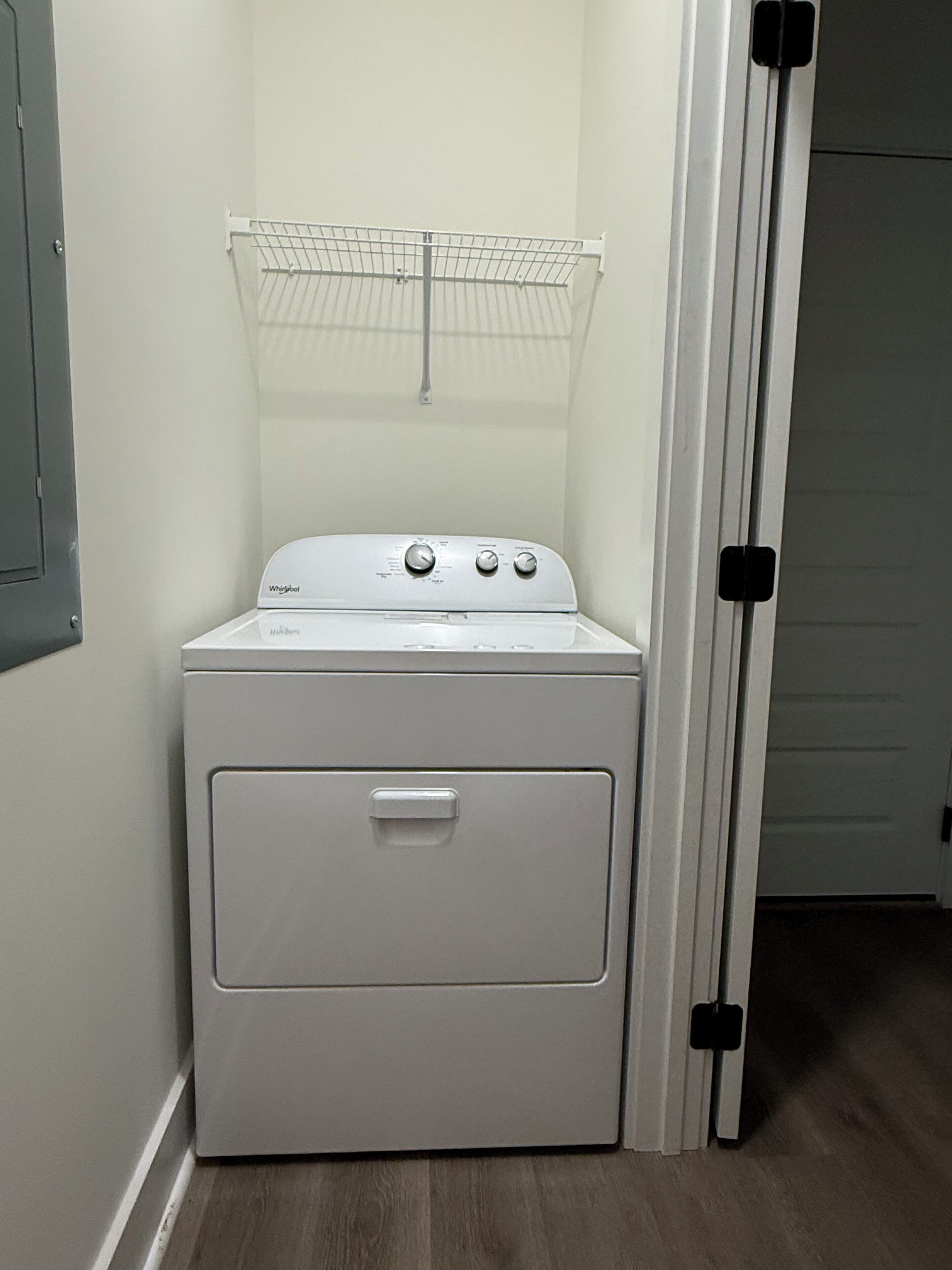Een compact, wit Whirlpool was- en droogcombinatie met een voorlaadontwerp, geplaatst in een hoek van een kamer met houten vloeren en een witte deur.