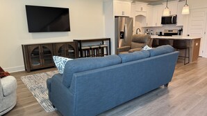 Ein modernes Wohnzimmer mit einem blauen Sofa, einem Flachbildfernseher und einer Küchenzeile inklusive Kühlschrank, Mikrowelle und Barhocker.