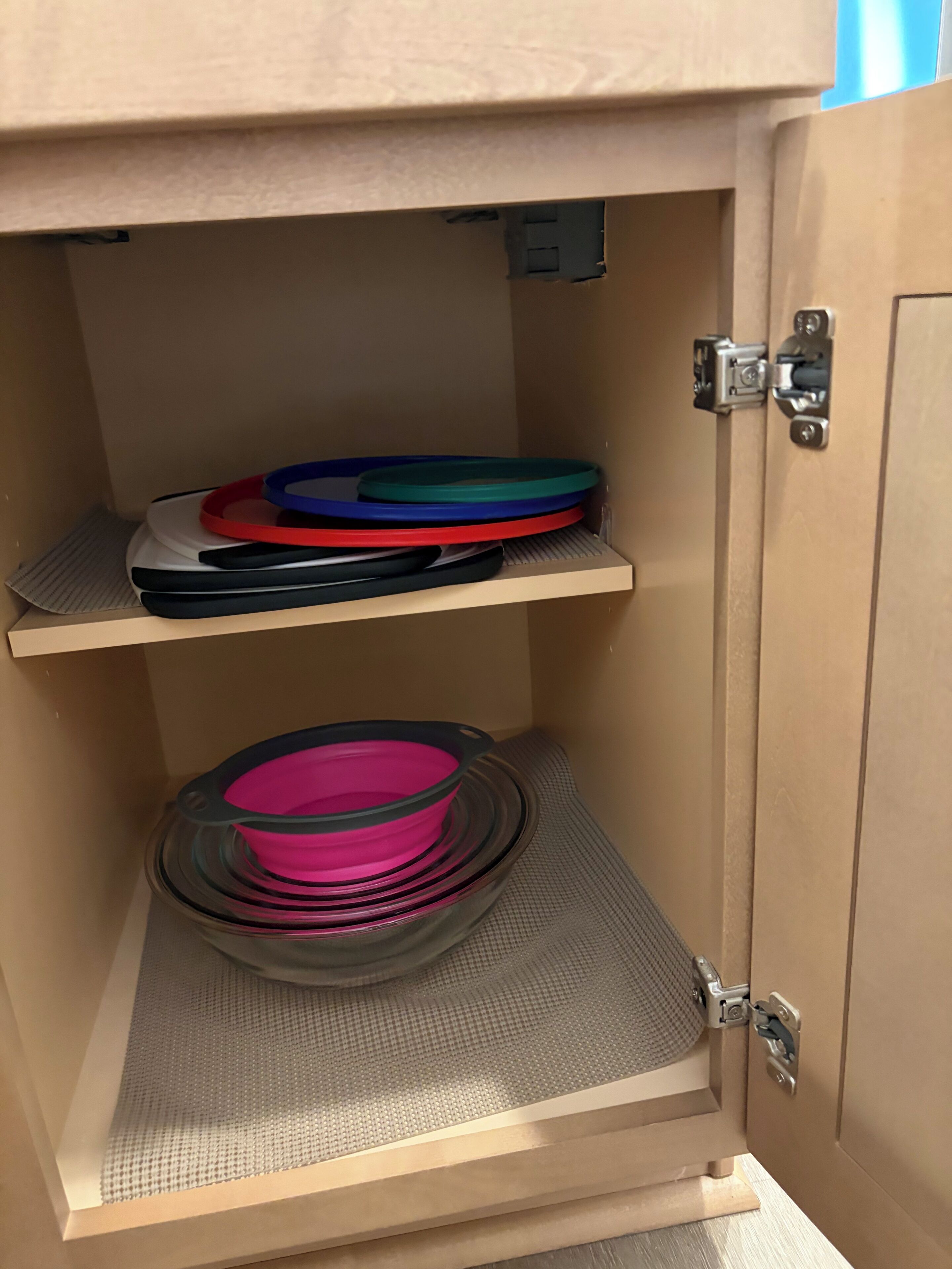 A cabinet with two shelves, one holding black and red plates, the other pink bowls.