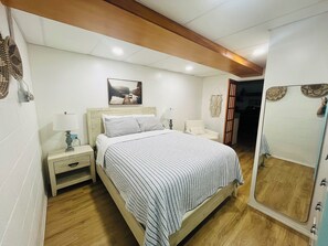 A bedroom with a bed, bedside tables, a nightstand, a chair, a mirror, and a door leading to another room. - Charming  1-bedroom apartment in peaceful Dayton with WiFi, AC. (Dayton)