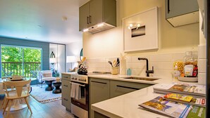 A modern kitchen with a large window, a dining area with a table and chairs, and a view of greenery outside. - Angani Studio - Elkhorn Resort Amenities Included (Sun Valley)