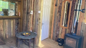 A rustic cabin interior with a wooden floor, a round table with a decorative bowl, a black stove, and a mirror on the wall. - Treehouse Cabin Wilderness Escape (Abergele)