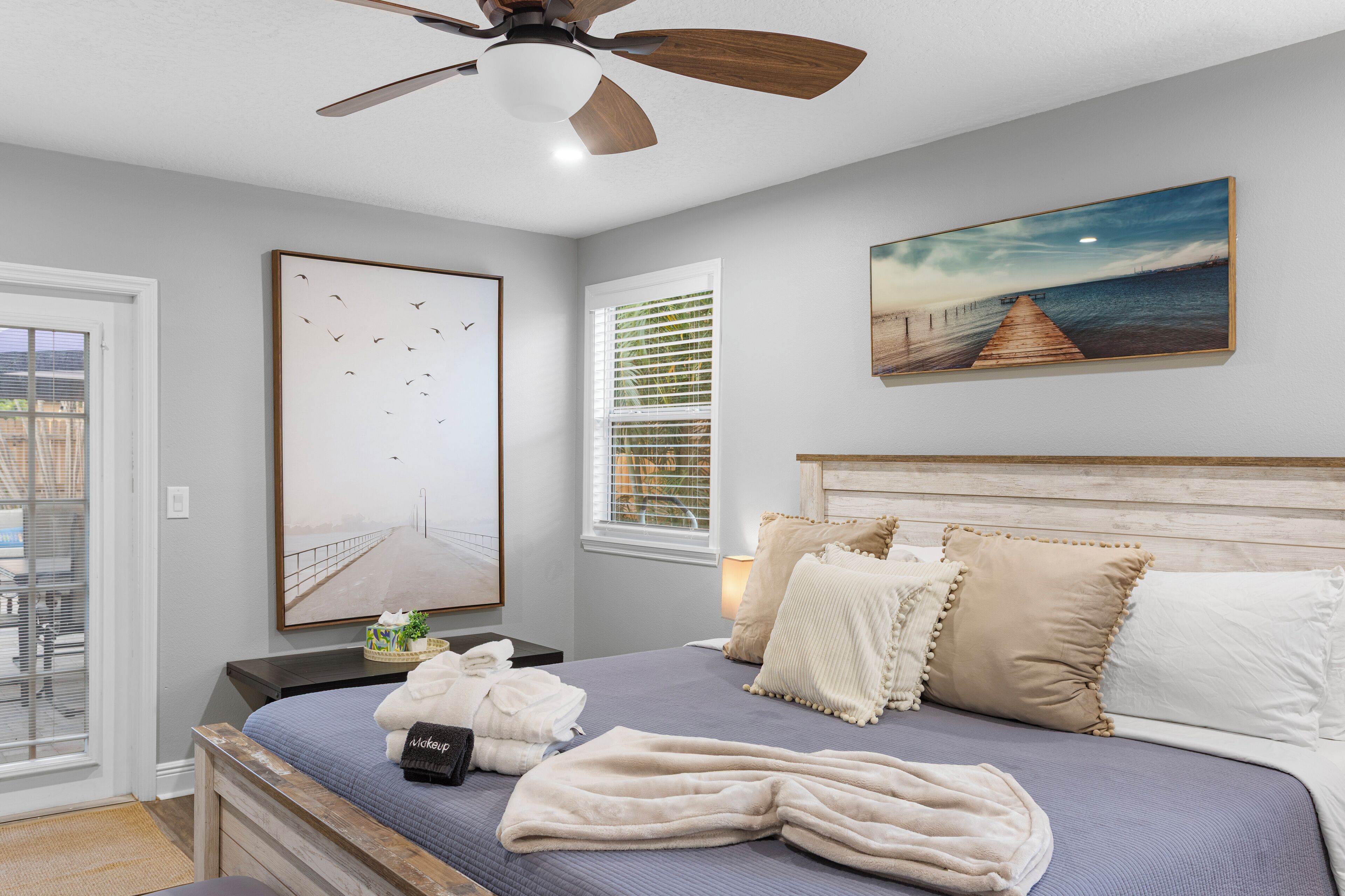 Un dormitorio con una cama, un ventilador de techo, una ventana con persianas y un cuadro en la pared.
