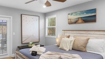 Un dormitorio con una cama, un ventilador de techo, una ventana con persianas y un cuadro en la pared.