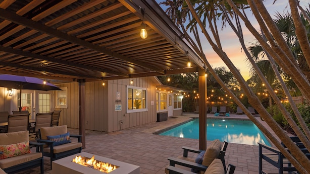 An outdoor patio with a pool, lounge chairs, a fire pit, and string lights.