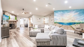 A spacious living room with a large sectional sofa, a fireplace, and a beach-themed mural on the wall.